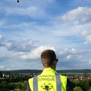 Drohnenpilot Stefan Vones, über ihm am leicht bewölkten Himmel eine Drohne