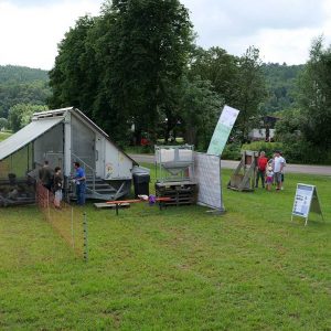 mobiler Hühnerstall und einige Personen auf einer Wiese