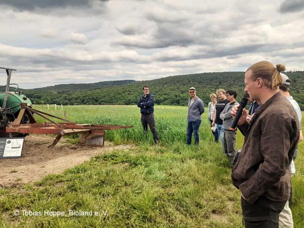 Personengruppe in einem Agroforstsystem, Mann ganz rechts mit Mikrofon; Foto: © Tobias Hoppe, Bioland e. V.