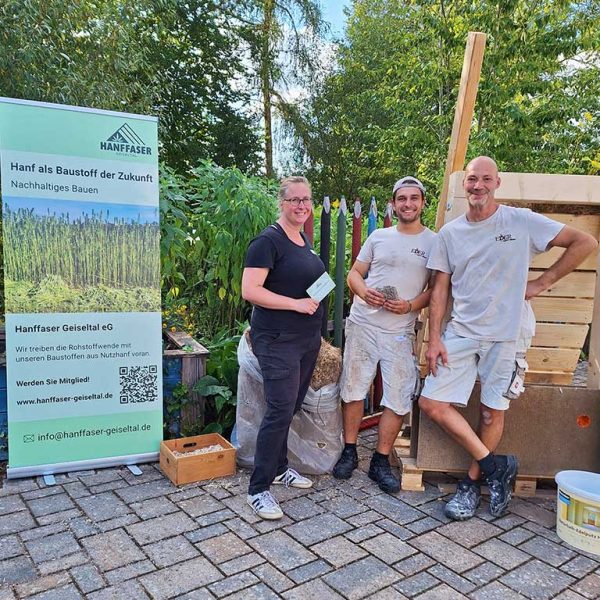 Drei Personen, die den Einbau von Hanfmaterialien in eine Wandkonstruktion präsentiert haben, stehen vor der Demonstrationswand