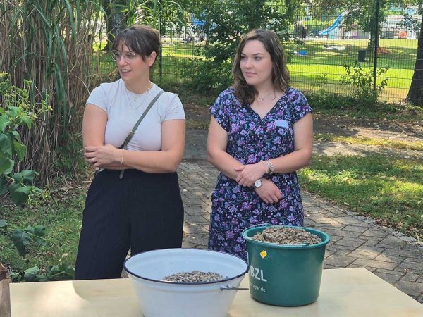 Zwei Frauen stehen hinter einem Tisch, auf dem Eimer mit Hanfstroh-Pellets stehen