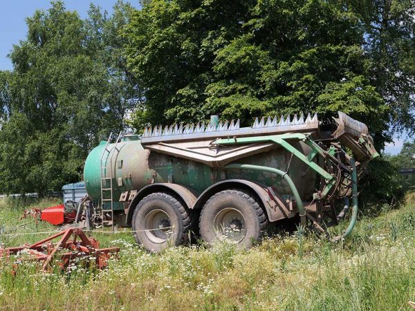 Schleppfix, ein Gerät zur Gülleausbringung steht auf einer Wiese; im Hintergrund Bäume