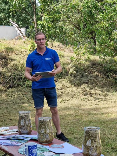 Ein LLH-Mitarbeiter steht auf einer Wiese und hat ein Tablett in der Hand; vor ihm ein Tisch mit Silageproben in Weckgläsern und Prospekte; © Silvia Matray