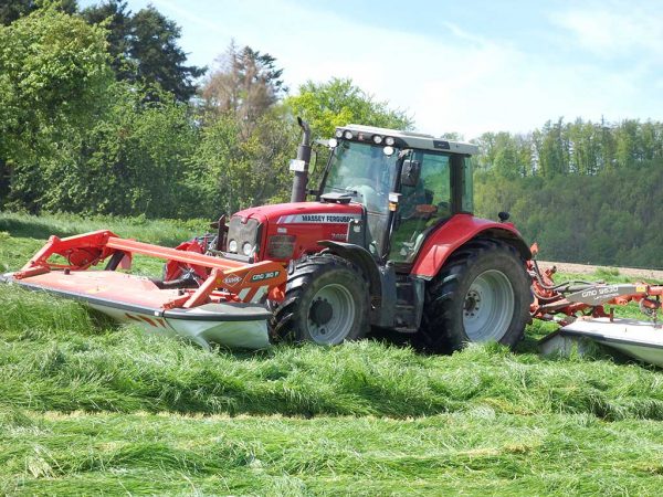 Ein Landwirt mäht mit einem Schlepper den ersten Aufwuchs des Grünlands