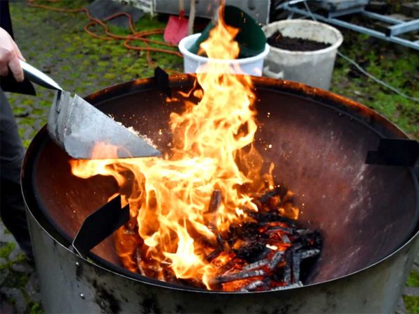 Abb. X: Ein Feuer aus Wabentrester und Holzrähmchenresten im Pyrolyseofen. Mit einer Handschaufel werden kleine Portionen nachgelegt.