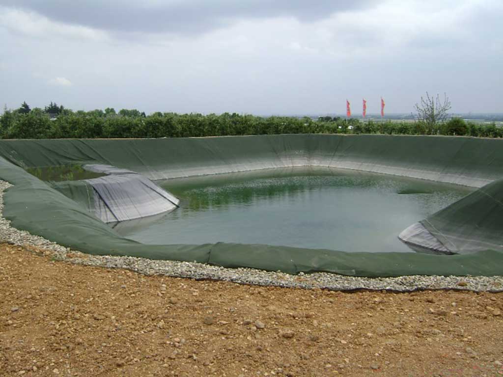 Frisch angelegtes, mit Folie ausgelegtes Wasserspeicherbecken, im Hintergrund sind Bäume, es ist bewölkt