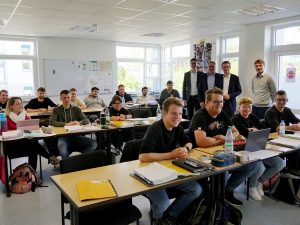 Blick in einen Klassenraum einer Fachschule; an drei Tischreihen sitzen die Studierenden; im Hintergrund stehen 4 Personen