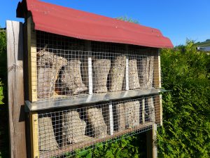 Zweistöckiges Insektenhotel mit rotem Dach, welches mit angebohrten Holzklötzen bestückt ist.