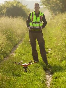 Person steht auf einem Feldweg und hält eine Fernsteuerung in der Hand Feldweg: vor der Person steht eine startende Drohne