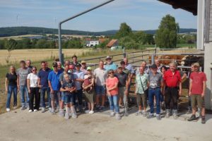 Exkursionsgruppe vor Auslauf, im Hintergrund Dorfbebauung und Felder
