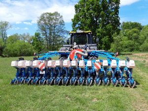 Blaue, pneumatische Drillmaschine auf einer Wiese, im Hintergrund sind Bäume