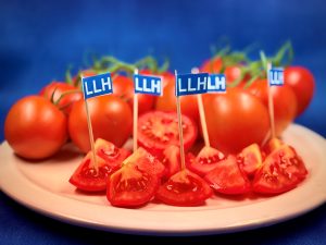 Aufgeschnittene rote Tomaten auf einem Teller, teilweise mit LLH-Fähnchen