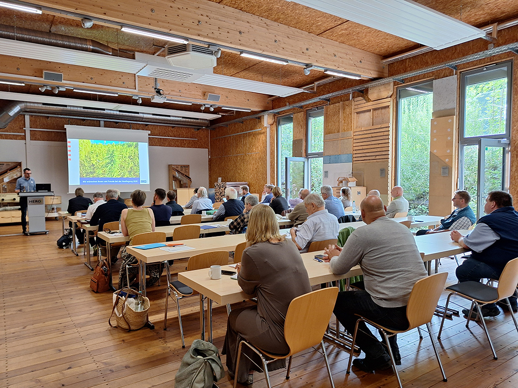 Seminarteilnehmende im Vordergrund, Referent Lukas Sittel am Pult mit PowerPoint im Hintergrund