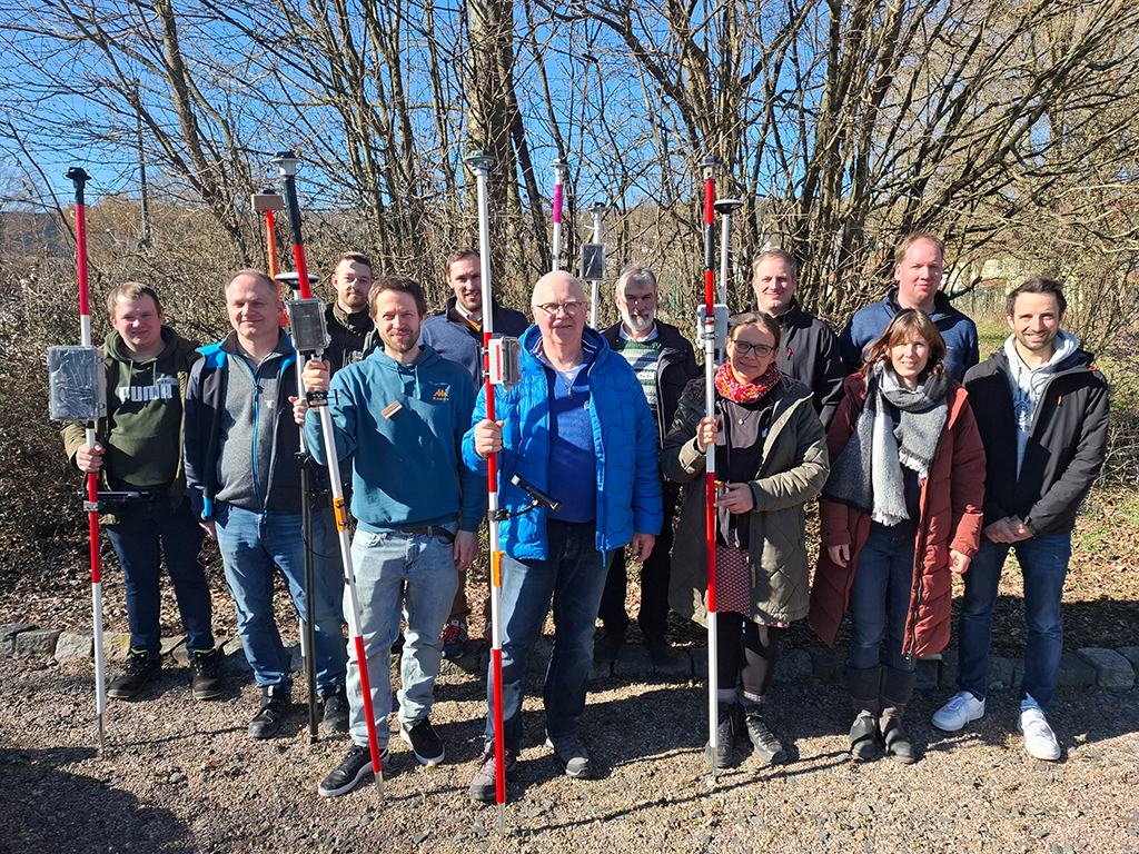 Eine Personengruppe vor unbelaubten Bäumen im Winter. Die Personen halten ihre selbstgebauten GNSS-Vermessungsstäbe in der Hand.