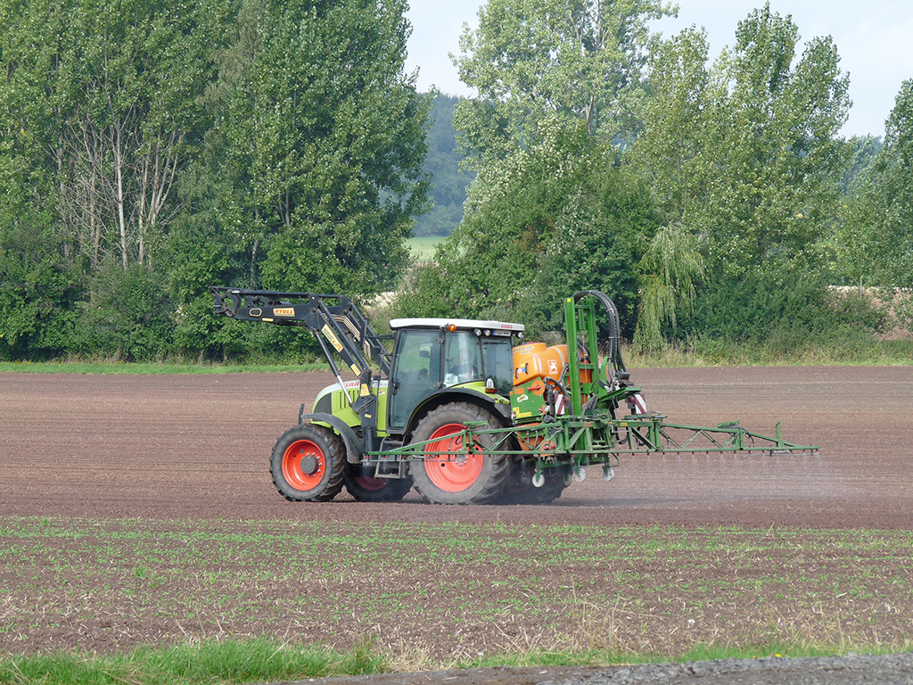 Pflanzenschutzanwendung auf einem Feld, im Hintergrund sind Pappeln.