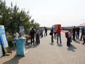 Das Foto zeigt kleine Stände im Freien. Aussteller präsentieren sich mit Stehtischen und Roll-ups. Besucher schauen sich um und sprechen mit ihnen. Die Sonne scheint.