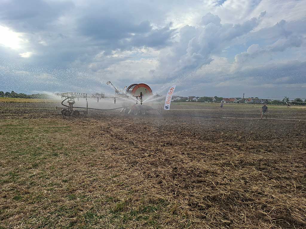 Das Foto zeigt eine Beregnungsmaschine mit Düsenwagen der Firma Beinlich im Einsatz. Feine Wasserstrahlen treten aus den Düsen aus.