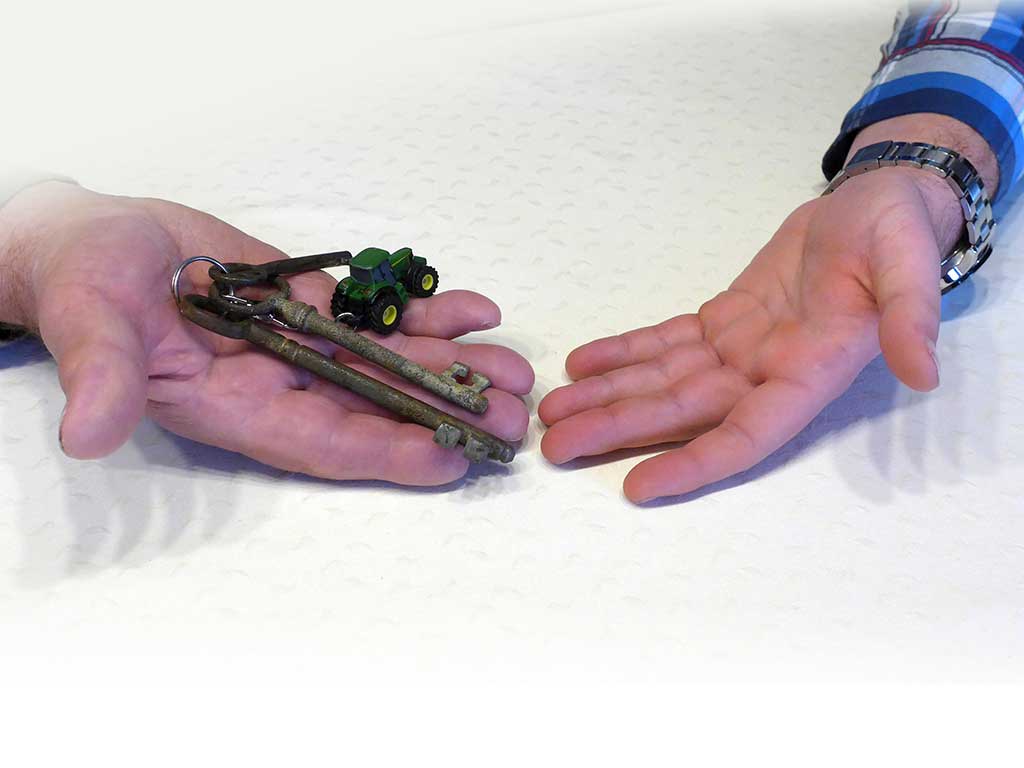 2 Hände; die linke Hand hält ein Schlüsselbund mit alten Schlüsseln und einen Spielzuegtrecker