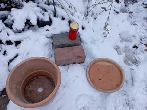 Materialien zum Bua einer Vogeltränke liegen im Schnee: Pflastersteine, Grabkerze, Blumentopf, Untersetzer