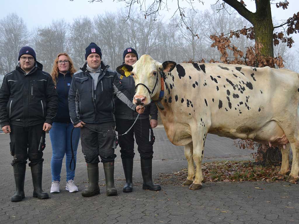 Vier glückliche Menschen stehen vor einer nebligen Waldkulisse. Eine Person hält eine weiße Kuh am Führstrick.