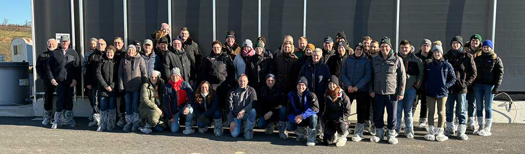 Gruppenfoto von Menschen bei Tageslicht, die frontal in die Kamera schauen. Im Hintergrund sind schwarze Windnetze zu sehen.