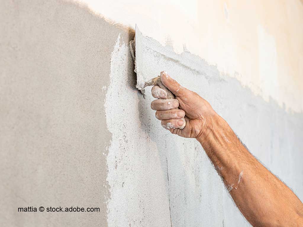 Hand einer Person, die mit einer Kelle Kalkputz auf eine Wand aufträgt