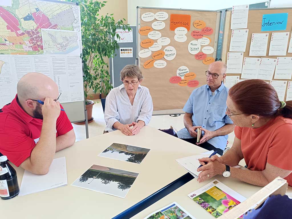 Man sieht vier sitzende Menschen, die sich anhand von Ausdrucken beraten wie eine Fläche aufgewertet werden kann.