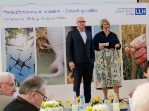 Ein Herr und eine Dame auf einer Bühne, im Hintergrund eine Leinwand.