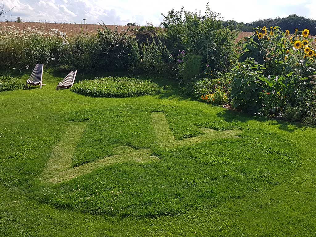 Rasen in einem Garten in den eine "44" hineingemäht wurde; im Hintergrund 2 Liegestühle