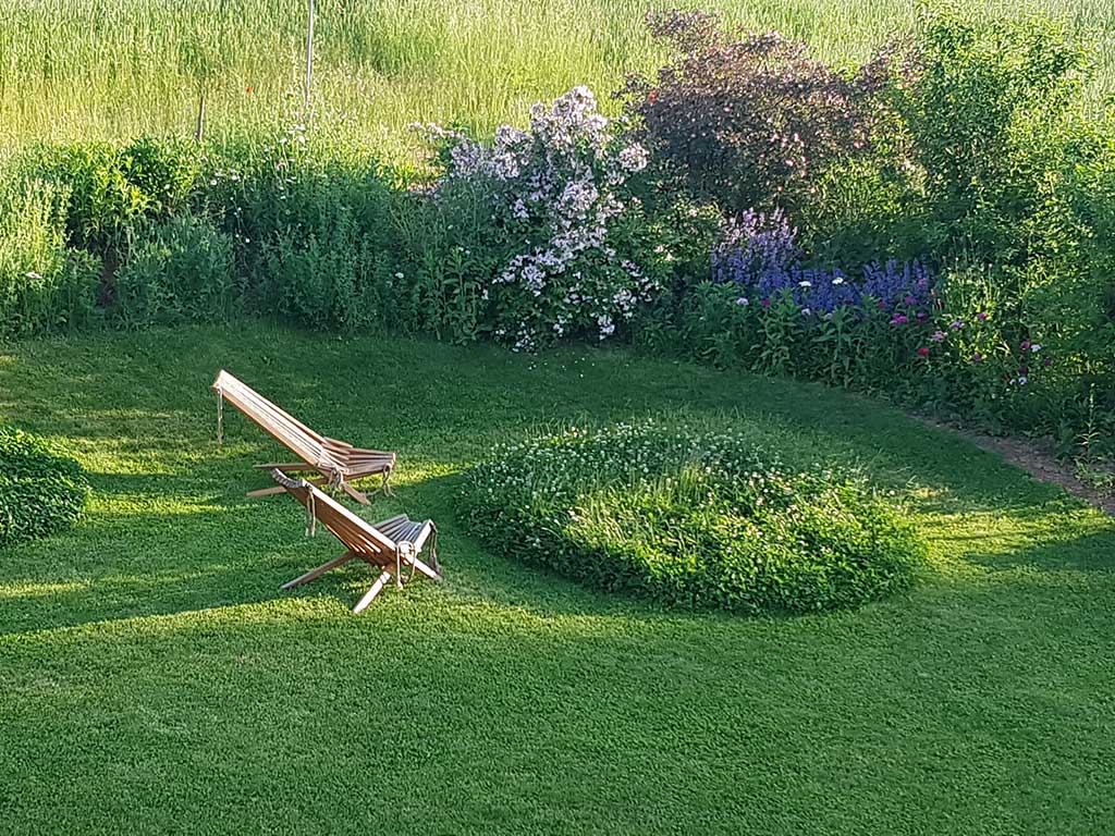 ein gemähter Rasen mit 2 Liegestühlen, auf dem ungemähte Inseln stehen gelassen wurden