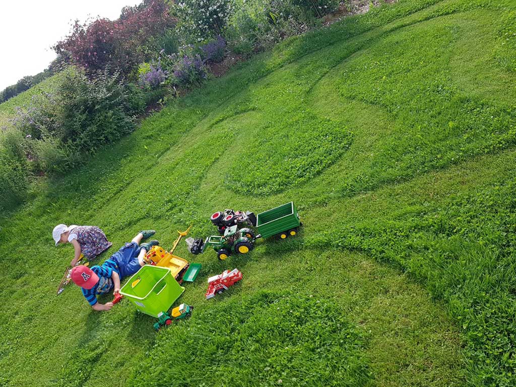 Spielende Kinder auf einem Rasen im Garten; in den Rasen sind geschwungene Linien gemäht