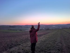 Eine Frau steht bei Sonnenaufgang auf einer Rebhuhn-Fläche und hält eine Klangattrappe in der Hand.