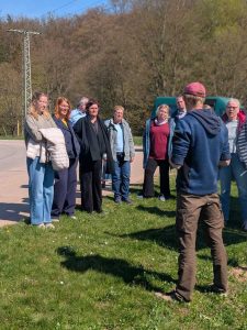 eine Personengruppe steht am Rand einer Wiese und informiert sich beim einem Rundgang