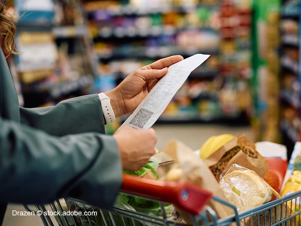 gefüllter Einkaufswagen; Kassenbon wird in den Händen gehalten