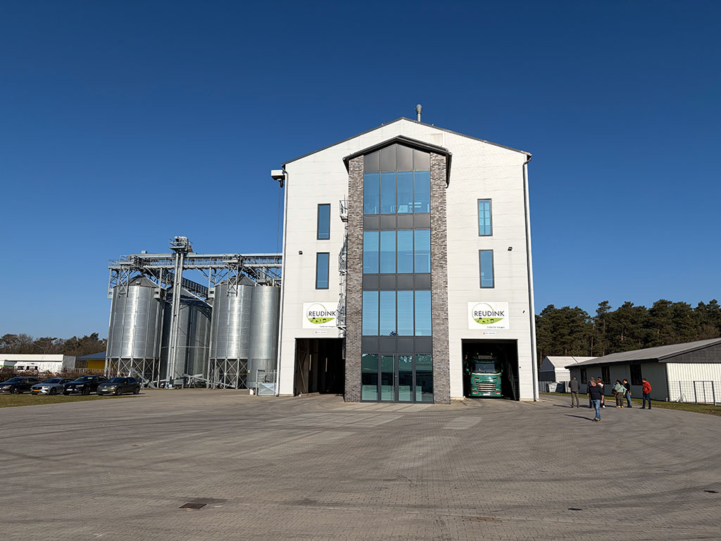 Ein riesiger, gepflasterter Rangierplatz und der strahlend blaue Himmel rahmen das moderne Futtermittelwerk mit seiner Glasfront und den nebendran stehenden Futtersilos ein.