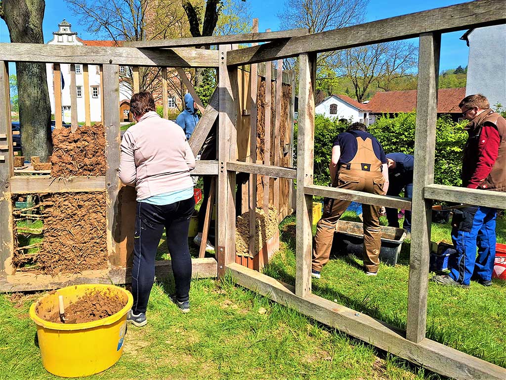 Teilnehmende des Praxis-Workshops „Lehmbau erleben“ am Landwirtschaftszentrum Eichhof arbeiten gemeinsam an einer Lehmbauwand. Unter fachlicher Anleitung werden Lehmbausteine hergestellt und das Ausfachen sowie Verputzen mit Lehm praktisch erprobt.