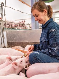 Eine junge Frau hockt zwischen Ferkeln in einem Stall.
