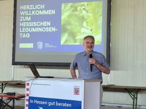 Redner mit Mikrofon an einem Rednerpult; im Hintergrund ein Präsentationsmonitor