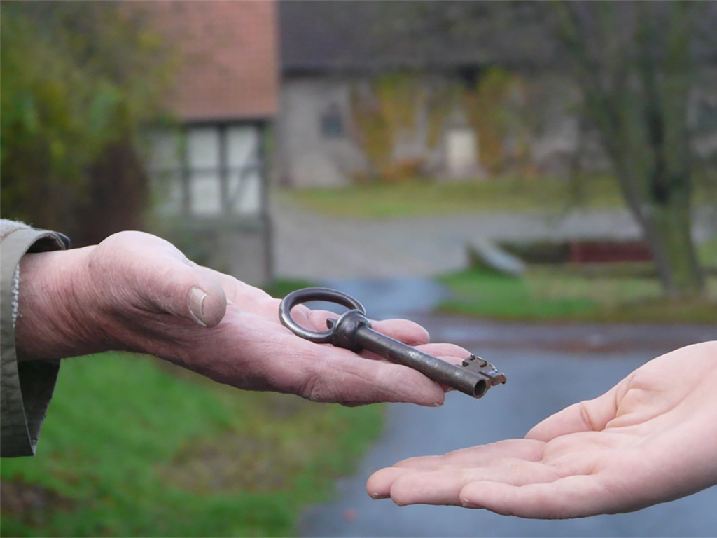 Hand eines älteren Mannes übergibt einen Schlüssel in eine 