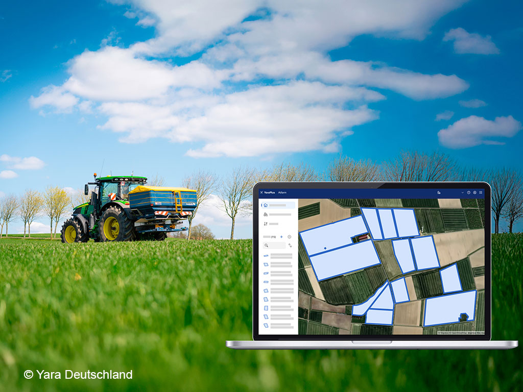 Trecker mit Düngerstreuer auf einer landwirtschaftlichen Fläche; im Vordergrund werden auf einem Tablet Flächen angezeigt