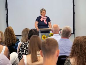 Rednerin an einem Pult; im Vordergrund Zuhörer