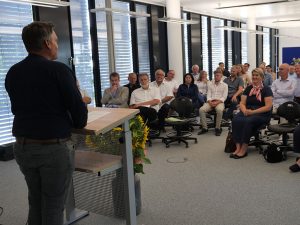 Redner an einem Pult in einem Klassenraum vor Zuhörern, die auf Stühlen sitzen