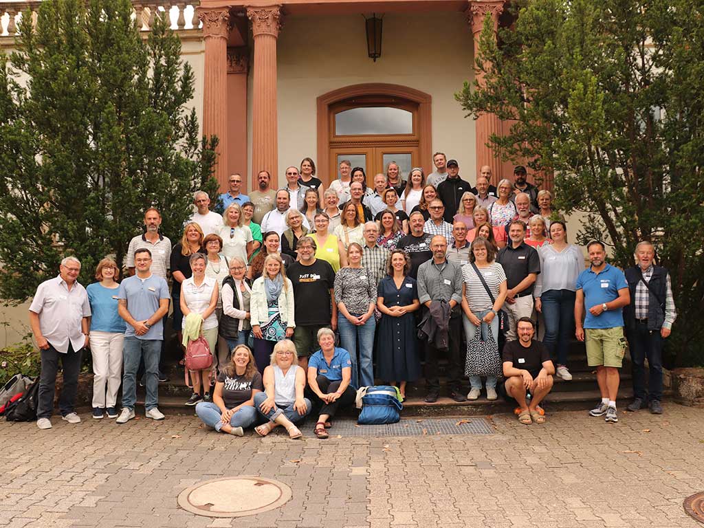 Gruppenfoto. Die Teilnehmenden, Referenten und das Team der Hessischen Gartenakademie stehen zusammen auf der Treppenanlage vor dem Haupteingang der Villa Monrepos. Die meisten Personen lachen, einige winken in die Kamera.
