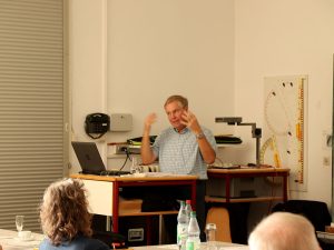 Der Referent steht im Veranstaltungsraum hinter dem Rednerpult und unterstreicht seinen Vortrag mit Gesten.