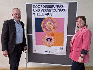 2 Personen stehen neben einem Flipchart mit einer Infografik mund lächeln in die Kamera.