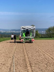 Trecker mit Sämaschine auf einer vorbereiteten Praxisfläche; 2 Personen stehen links daneben